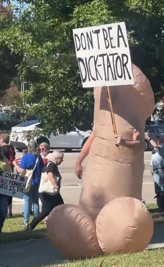 No Kings protest with someone dressed in a phallus costume holding a sign saying 'Don't be a dick-tator'